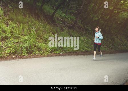 Una giovane donna bionda che corre si pratica all'aperto in un parco montano cittadino nella foresta. Raggi caldi attraverso i rami degli alberi Foto Stock