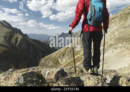 Il corpo dell'uomo con uno zaino e pali da trekking si erge sulla cima di una roccia sullo sfondo della valle rocciosa in alta montagna. Il concetto di t Foto Stock