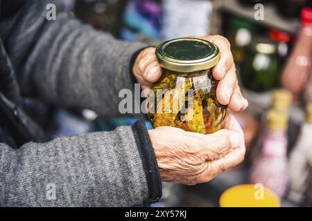Le vecchie mani stropicciate tengono in mano un barattolo con marmellata di montagna dalle foglie degli alberi caucasici nelle montagne Foto Stock