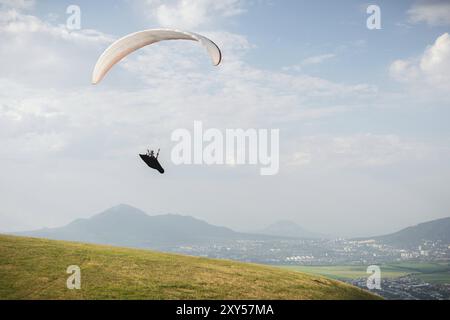 Un parapendio bianco-arancio vola sul terreno montuoso Foto Stock