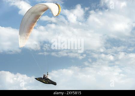 Il parapendio professionista vola su un parapendio bianco contro il cielo blu e le nuvole bianche. Sport di parapendio Foto Stock