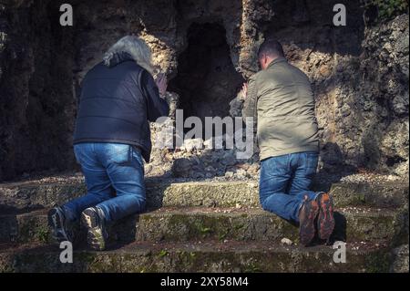 Due uomini inginocchiati in preghiera sui gradini di fronte a una grotta Foto Stock