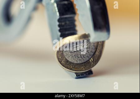 Un euro piegato tra le ganasce di un paio di pinze con curvatura concava Foto Stock