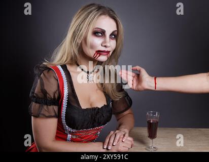 Donna bionda inventata come vampiro ad Halloween mentre beveva sangue dal braccio Foto Stock