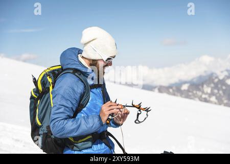 Una giovane guida con barba e occhiali da sole prepara i ramponi per l'uso Foto Stock