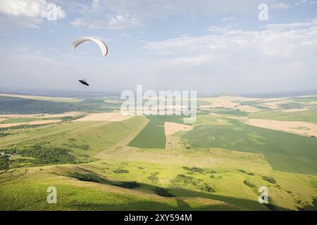 Un parapendio bianco-arancio vola sul terreno montuoso Foto Stock