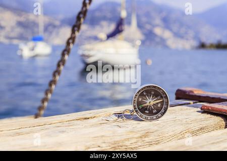 Compass giacente sul dock in legno pier in primo piano, barche a vela in sfondo sfocato Foto Stock