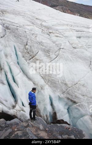 Il viaggiatore in una cuffia e gli occhiali da sole sta in piedi nelle montagne innevate sul ghiacciaio. Viaggiatori in un ambiente naturale Foto Stock
