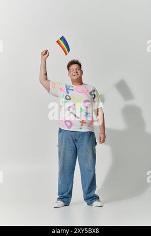 Un giovane sorride con gioia, tenendo in alto una bandiera arcobaleno. Foto Stock
