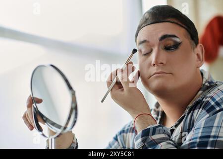 Una persona queer applica l'ombra, il cui riflesso è visibile in uno specchio. Foto Stock