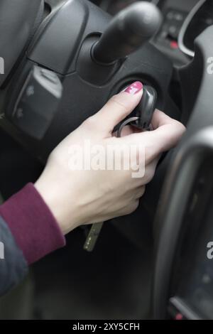 Primo piano interno veicolo di mano in possesso della chiave di accensione, il volante e il nero di fondo interna femmina, il concetto di driver Foto Stock