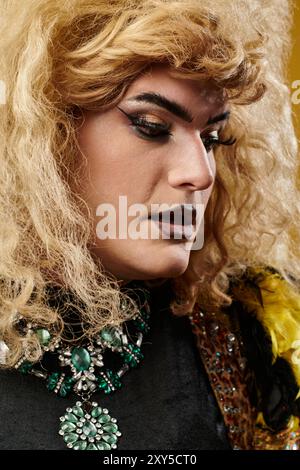 Una persona queer bionda in un trucco spettacolare guarda verso il basso, indossando una collana color smeraldo Foto Stock