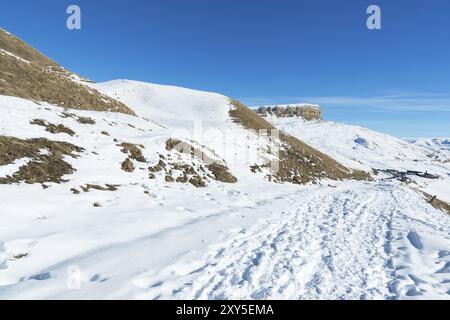 Il paesaggio di rocce caucasiche innevate sul passo Gumbashi. Altopiano innevato che passa nella montagna da tavola con un sentiero innevato in avanti Foto Stock