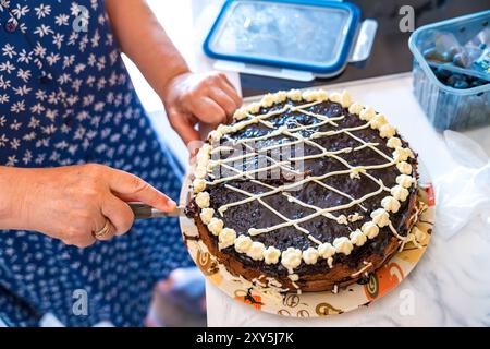 Il processo di taglio da vicino di una torta al cioccolato fatta in casa da una donna anziana nella cucina di casa Foto Stock