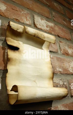 Vecchio pezzo di pergamena con bordi bruciati su un muro di mattoni, sfondo grintoso Foto Stock