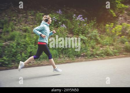 Una giovane donna bionda che corre si pratica all'aperto in un parco montano cittadino nella foresta. Raggi caldi attraverso i rami degli alberi Foto Stock