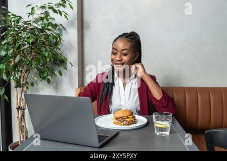 Giovane donna d'affari che lavora a distanza dalla caffetteria durante la pausa pranzo. Lavoratrice in ufficio che utilizza un computer portatile mentre mangia al ristorante Foto Stock