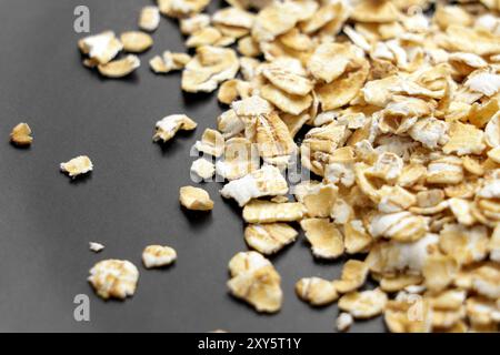 Fiocchi d'avena organici nel piatto nero della cucina da vicino. Cereali crudi di farina d'avena. Ingrediente cerealicolo sano Foto Stock
