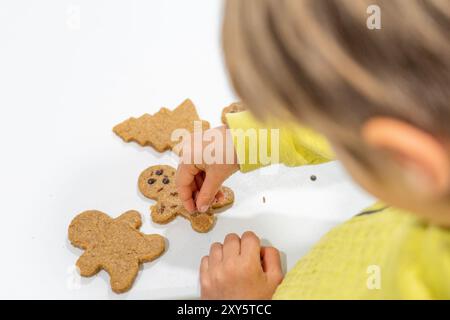 Bambino irriconoscibile che decora biscotti fatti in casa con pan di zenzero e gocce di cioccolato Foto Stock