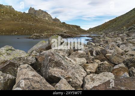 Paesaggio notturno di un lago di alta montagna al chiaro di luna con enormi pietre in primo piano e scogli appuntiti sullo sfondo Foto Stock