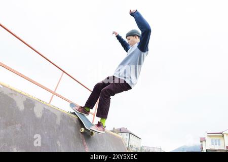 Skater adolescente in felpa con cappuccio e jeans scivola su una ringhiera su uno skateboard in uno skate Park, grandangolare Foto Stock