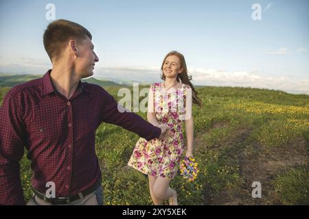 Giovane coppia sposata. Il tizio conduce una ragazza riccia con un mazzo di fiori. Il concetto di fiducia e famiglia giovane felice Foto Stock