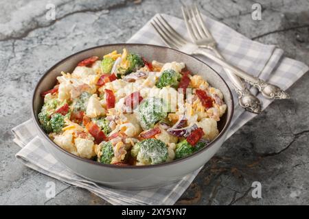 Deliziosa insalata di maionese con broccoli, cavolfiore, pancetta, formaggio cheddar e cipolla rossa da vicino in un recipiente sul tavolo. Orizzontale Foto Stock