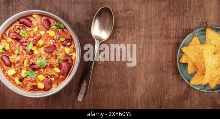 Un panorama di chili con carne con nachos, girato dalla parte superiore al buio su un rustico sfondo di legno con un posto per il testo, la cucina messicana del modello di progettazione Foto Stock