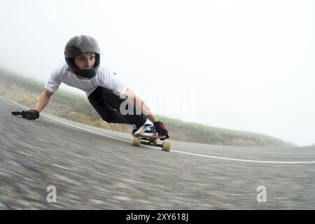 Un giovane con un casco integrale su una strada di campagna in uno scivolo passa una svolta su uno sfondo di nuvole basse e nebbia Foto Stock