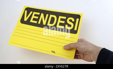 Cartello per la vendita dell'appartamento scritto in italiano, con la mano di un adulto che tiene in mano il bando, spazio per copia su sfondo bianco. Foto Stock