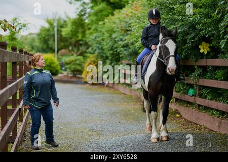 Ragazza, equitazione ed equitazione in campagna per equestre, sviluppo e apprendimento con istruttore. Adolescente, animale e animale domestico in fattoria per allenarsi e insegnare Foto Stock