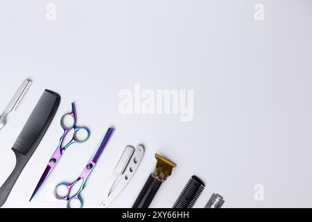 Vista dettagliata degli utensili da barbiere angolati disposti su sfondo bianco. Gli utensili, tra cui forbici e rasoi, sono ben posizionati sulla sinistra si Foto Stock