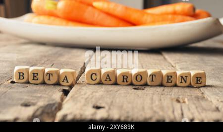 Dadi di legno con le parole il beta-carotene e le carote fresche nel retro, mangiare sano concetto Foto Stock