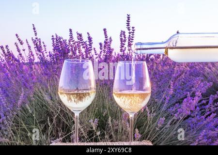 Vino di lavanda. Vino bianco versata da una bottiglia in bicchieri contro un campo di lavanda sfondo Foto Stock