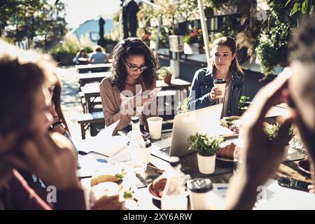 Persone, studenti e felici al ristorante per compiti di gruppo sul lavoro di squadra e la collaborazione. Caffetteria, amici e compagni di scuola universitari Foto Stock