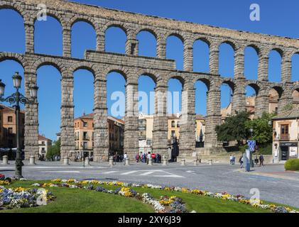 Un acquedotto storico con archi in pietra abbraccia una città con un'aiuola in primo piano sotto un cielo blu, acquedotto, Segovia, Castilla y Leon, Leon, SPAI Foto Stock