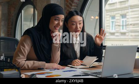 Due donne d'affari multirazziali donna asiatica coreana ragazza musulmana hijab islamico donna d'affari in ufficio video chiamata laptop conferenza virtuale Foto Stock