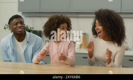 Famiglia afroamericana spensierata genitori birazziali etnici felici e una bambina carina che balla con la musica divertendosi insieme in cucina a casa Foto Stock