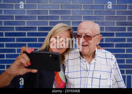 Ritratto di un padre più grande e di sua figlia sorridenti per la fotocamera mobile. Festa dei padri Foto Stock