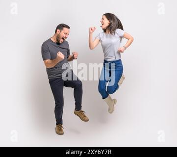 Tutta la lunghezza di giovani coppie eccitate che urlano e pompano pugni saltando su sfondo bianco Foto Stock