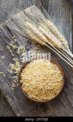 Spaghetti d'orzo crudi in ciotola su fondo in legno con affettati, concetto di cibo crudo Foto Stock