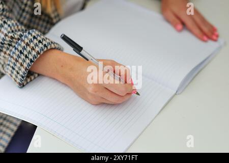 Giovane donna d'affari che scrive in blocco note mentre è seduta in ufficio. Mani femminili che tengono una penna e fanno appunti da vicino. Foto Stock
