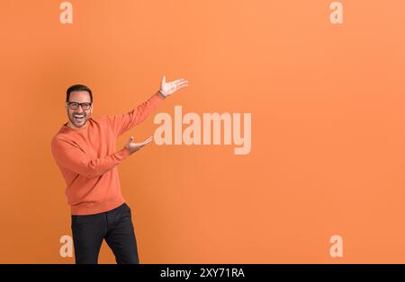Uomo d'affari estatico in occhiali da vista con le braccia alzate pubblicità su spazio di copia su sfondo arancione Foto Stock
