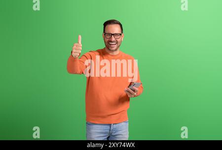 Ritratto di un giovane uomo d'affari sorridente che mostra segni e usa il telefono cellulare su sfondo verde Foto Stock