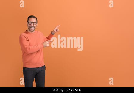 Ritratto del promotore maschio che ride e punta allo spazio di copia mentre marketing su sfondo arancione Foto Stock