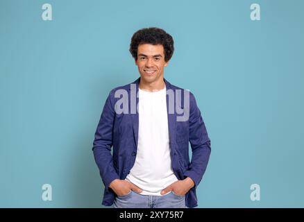 Ritratto di un uomo d'affari sorridente con acconciatura afro e tasche in posa su sfondo blu Foto Stock