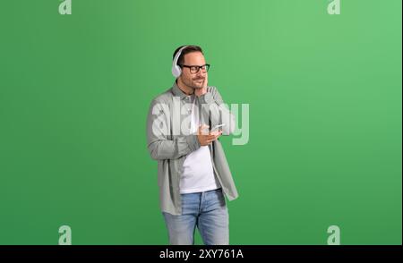 Uomo d'affari sorridente con gli occhi chiusi ascoltando musica con le cuffie e rilassandosi su sfondo verde Foto Stock