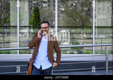 Imprenditore sorridente che discute strategie con il cliente telefonicamente contro la costruzione in città Foto Stock