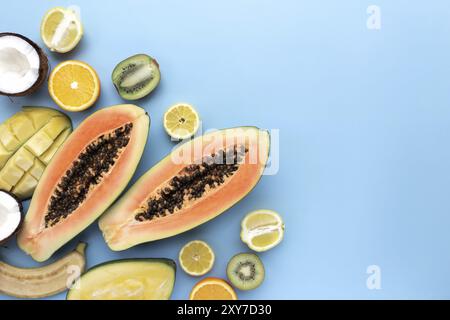 Diversi frutti freschi di taglio tropicale su sfondo blu. Papaya, arancio, banana, cocco, mango, kiwi e limone vista dall'alto piatto con spazio per la copia Foto Stock