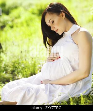 Ritratto di bella donna incinta in abito bianco nel Parco di primavera Foto Stock